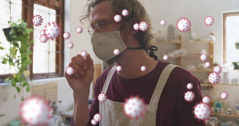Caucasian man coughing in mask at pottery workshop with covid-19 cells