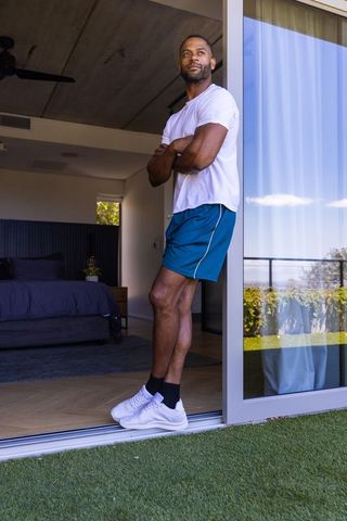 African american man standing at sliding glass door on balcony enjoying sunlight