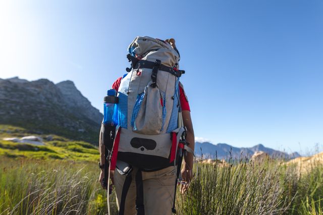 This image shows a fit, disabled athlete with a prosthetic leg hiking in a mountain field, carrying a backpack. It can be used to promote active lifestyles, outdoor adventures, and travel for people with disabilities. Ideal for websites, blogs, and campaigns focused on fitness, independence, and determination.