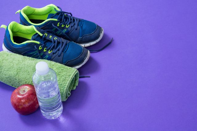 Water bottle, towel, apple and sneakers on purple background