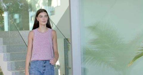 Woman walking through modern glass entry wearing pink tank and denim button-front skirt