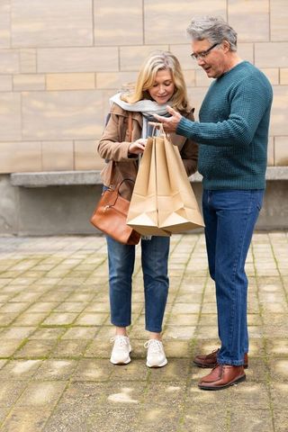 Senior couple shopping together holding brown paper bags in urban courtyard