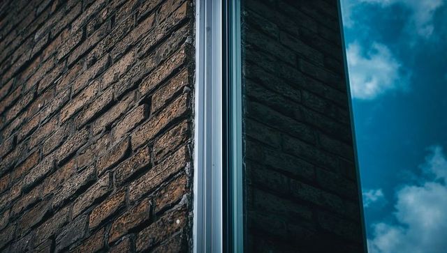 Showcasing weathered brick corner with metal trim and reflective glass reflecting blue sky