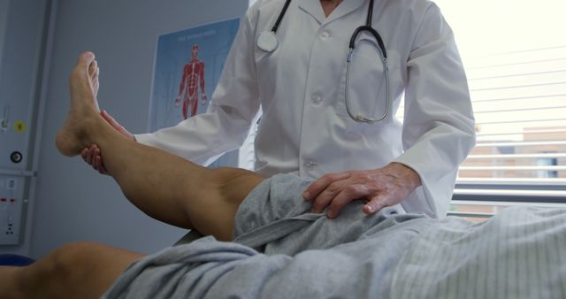 Doctor wearing white coat and stethoscope examining patient's leg in medical office. Useful for promoting healthcare services, physical therapy centers, medical examinations, rehabilitation programs, and clinical care guides.