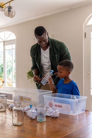 African american father and son sorting recyclables at home with plastic and glass bins