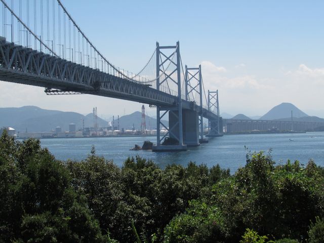 Perfect for travel magazines, tourism promotions, transportation articles, and stock imaginations of Japanese bridges. Stunning view of the Great Seto Bridge showcasing the impressive engineering and serene waterfront, providing contrast with industrial elements in background.