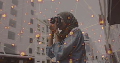 Hijabi Woman Capturing Photos with Overlay of Digital Network Icons