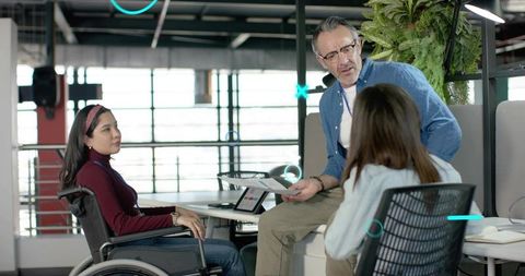 Inclusive team discussing project plans with wheelchair colleague in modern office