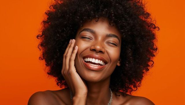 Radiant woman with natural curls smiling on vibrant orange backdrop, bare shoulders