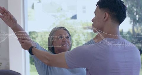 Caregiver guiding senior, assisting arm stretch at home with smartwatch monitoring