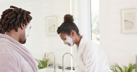 African american couple applying face masks in bright minimal bathroom