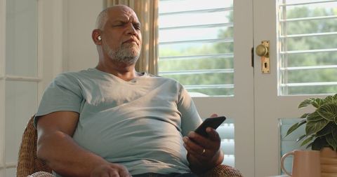 Senior Man Enjoying Music on Smartphone at Home in Sunlit Room