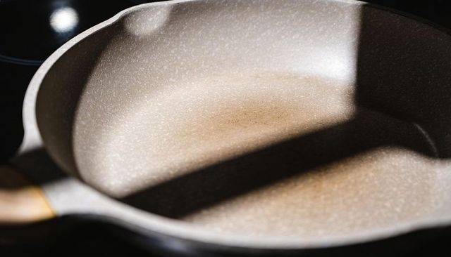 Sunlit speckled nonstick skillet resting on glass cooktop with gold handle and diagonal shadow