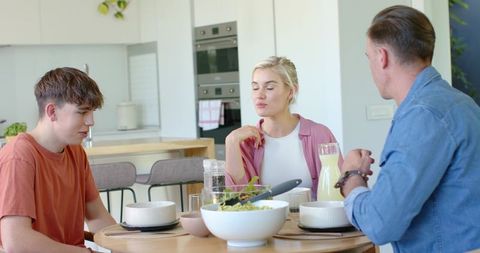 Family conversing over healthy salad in bright modern kitchen during casual morning meal