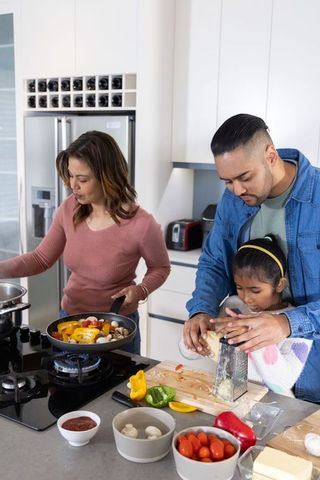 Family cooking together in modern kitchen while father teaching daughter to grate cheese