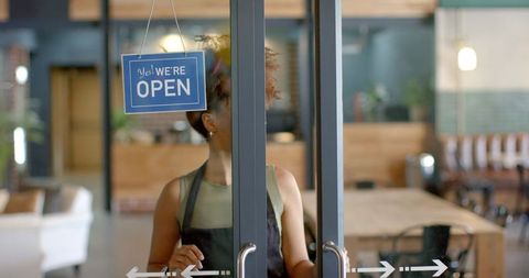 African american barista opening glass door of cozy contemporary cafe with open sign