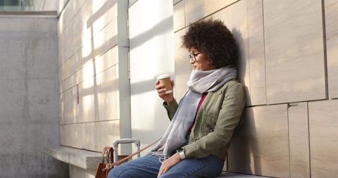 African american woman relaxing with coffee while waiting at urban transit plaza