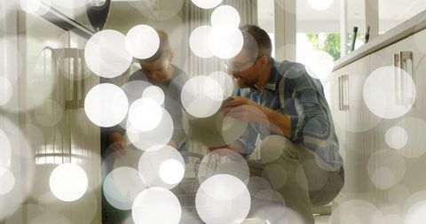 Father guiding young son loading dishwasher at home with bokeh light overlay teaching teamwork