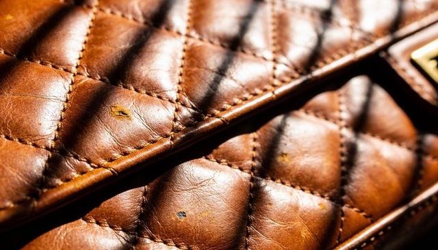 Quilted brown leather purse flap showing diamond stitch, patina scuffs, striped sunlight
