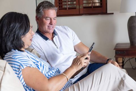 Senior couple sharing smartphone on sofa, relaxing at home and browsing photos together