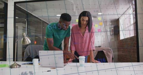 Collaborating colleagues reviewing notes and laptop in modern creative office