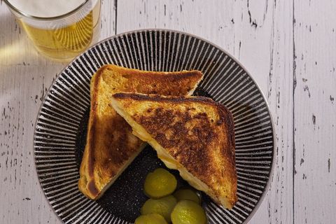 Golden grilled cheese sandwich with pickles on striped ceramic plate, rustic breakfast