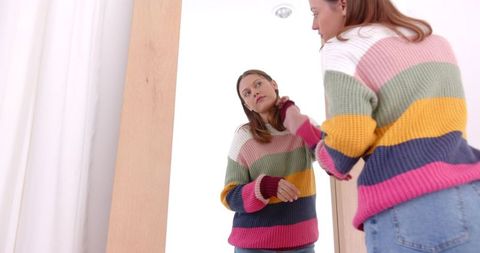 Woman reflects in mirror adjusting colorful sweater