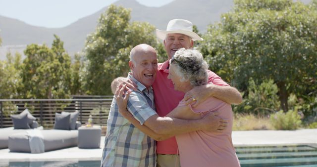 Two elderly men and an elderly woman hugging and smiling in a garden setting with mountains in the background. Use for themes like friendship, retirement lifestyle, happiness and outdoor activities among senior citizens.