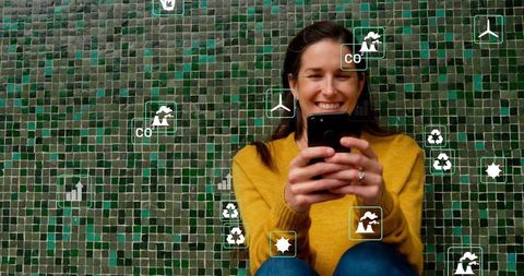 Smiling woman holding smartphone using sustainability app with green mosaic background