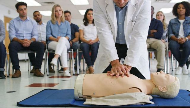 Medical instructor performing cpr training on mannequin in classroom with students