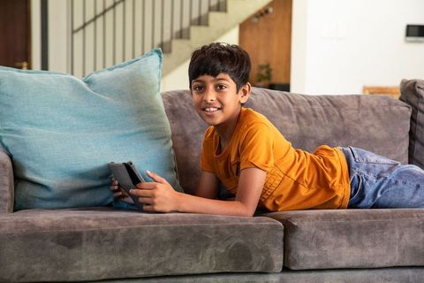 Indian boy relaxing on sofa with gaming device