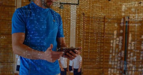 Coach holding tablet supervising children training in school gymnasium with code overlay