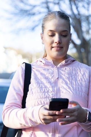 Young woman checking smartphone while commuting in pink quilted jacket and smartwatch