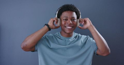 Smiling young man adjusting wireless over-ear headphones wearing casual blue tee