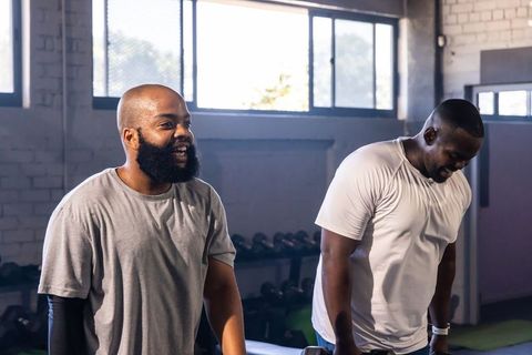 African men working out together lifting dumbbells in industrial gym with sunlight