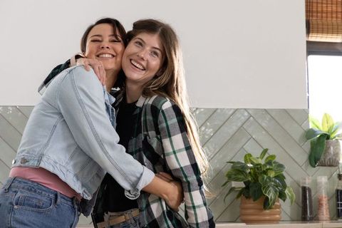 Friends hugging and smiling in sunlit kitchen with cozy tile backsplash and plants