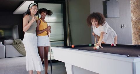 African american women playing pool and laughing in modern lounge with drinks