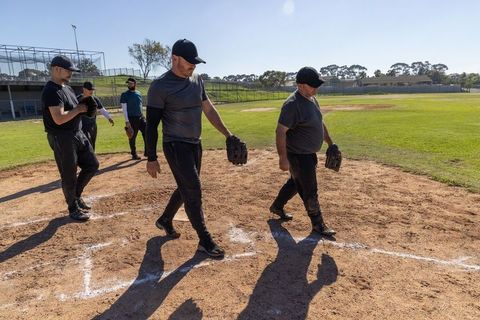 Adult baseball teammates walking across infield holding gloves during sunny team practice