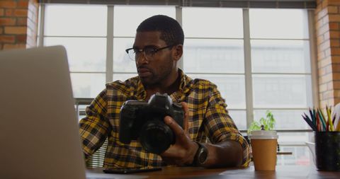 Man Checking Photos on Camera While Editing at Office Desk