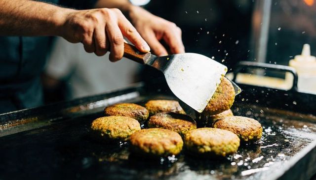 Flipping veggie patties on hot flat-top griddle with metal spatula, sizzling action