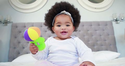 Adorable Baby with Afrofro Munching on a Toy in Bright Bedroom