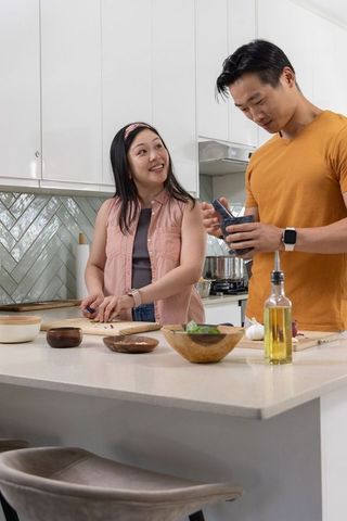 Diverse couple cooking together at modern kitchen island chopping vegetables and seasoning