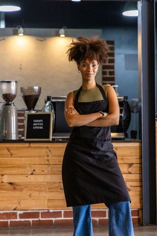 Confident african american barista standing with arms crossed in warm rustic coffee shop