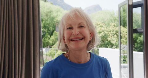 Smiling senior woman posing by open balcony door in bright room