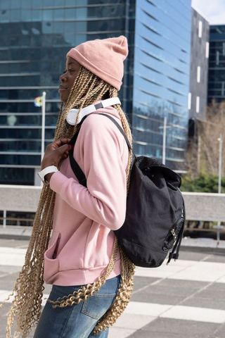 African american woman walking plaza wearing pink beanie long braids backpack headphones