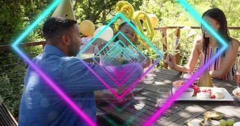 Friends celebrating on wooden deck patio with neon overlay and gold balloons