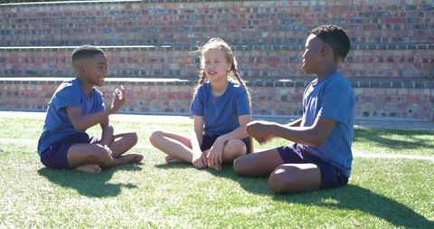 Multicultural teens sitting barefoot on school lawn sharing conversation and laughter