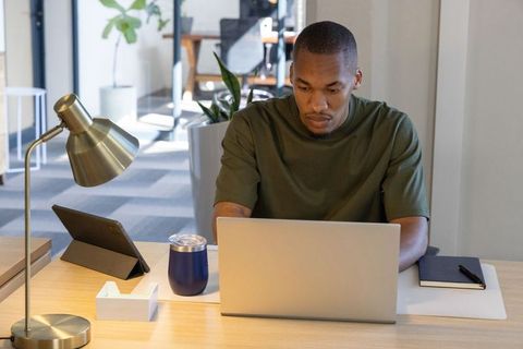 African american man working on laptop at modern coworking desk with tablet, notebook