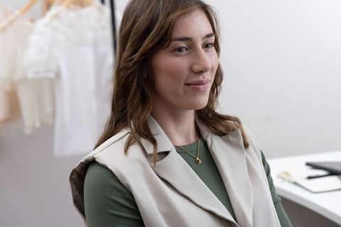 Fashion designer consulting client in minimal atelier wearing beige vest and gold necklace