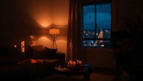 Cozy living room at night with warm floor lamp, candles and city bokeh through window